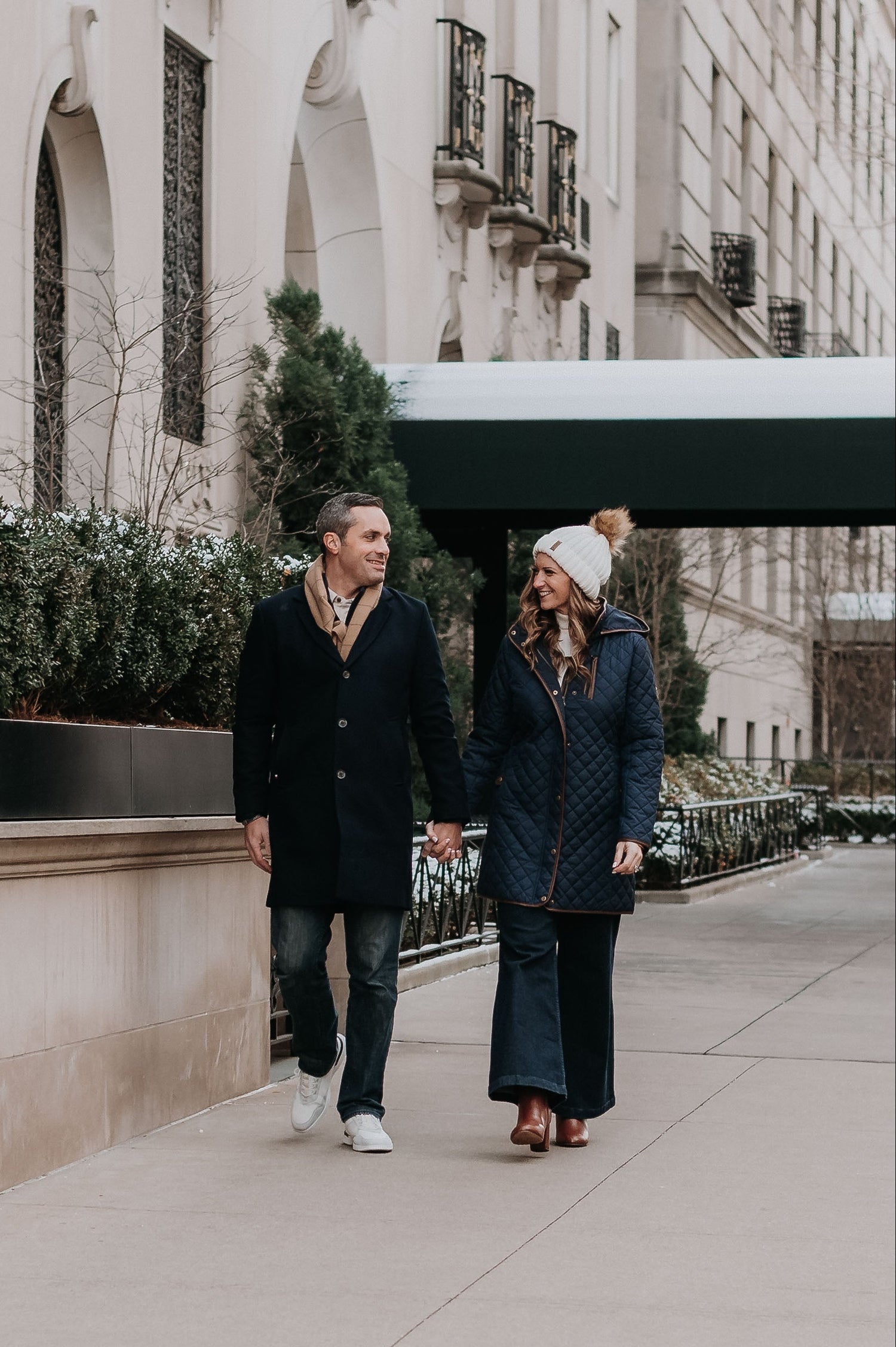 Couple walking hand-in-hand on a city sidewalk with a building in the background