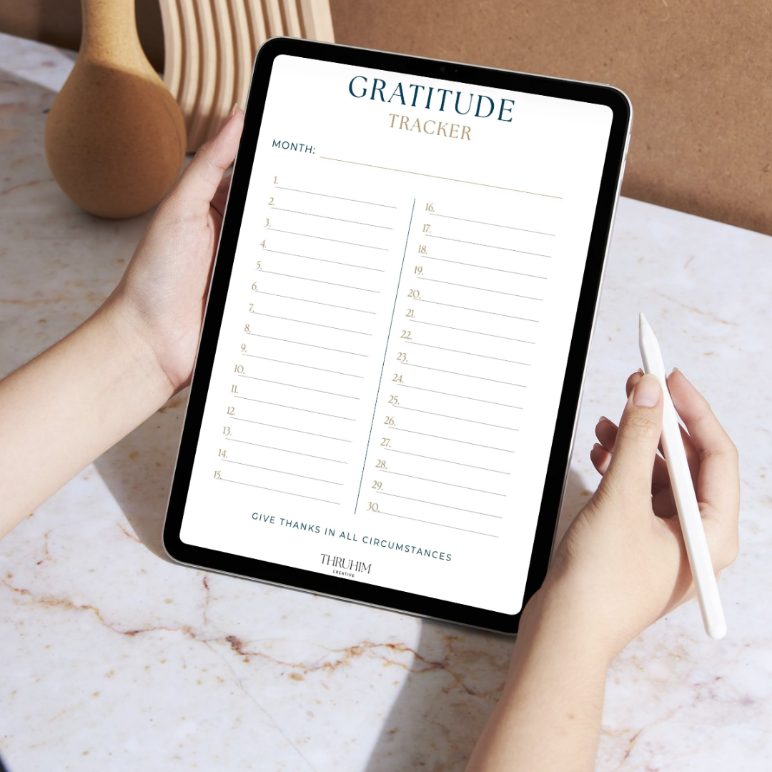 Person holding a tablet displaying a gratitude tracker worksheet on a marble surface