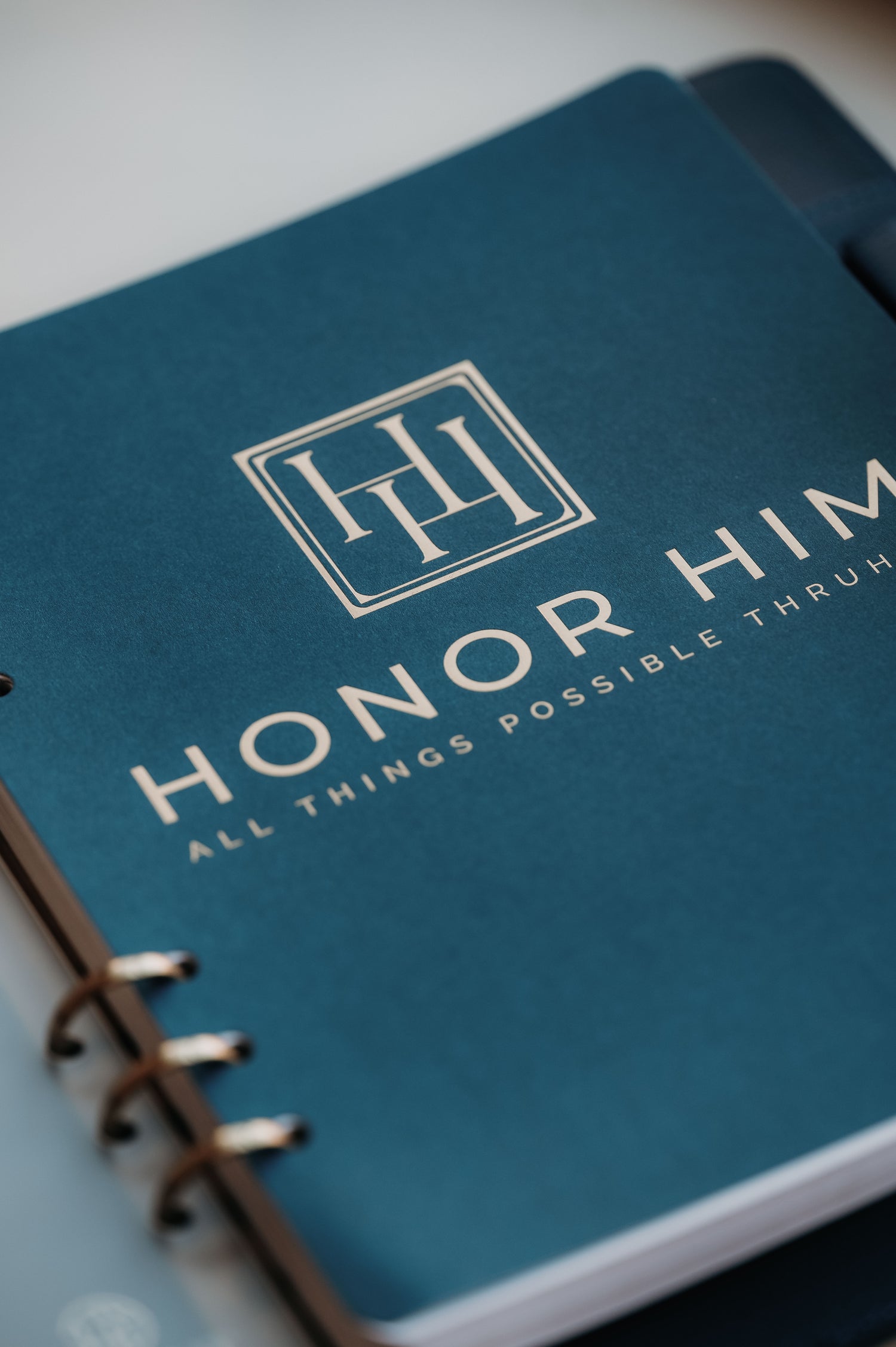 Close-up of the Honor Him Christian marriage planner featuring the ThruHim Creative logo on a premium navy vegan leather planner cover.